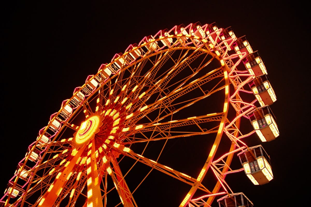 A Ferris wheel lit by orange lights spins at night.