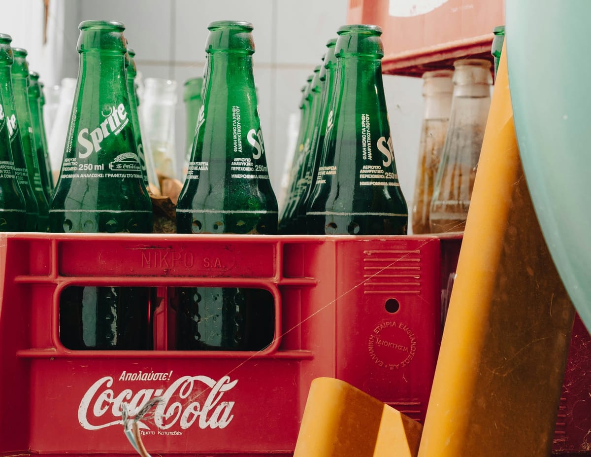 Close-up of green Sprite glass bottles in a red Coca-Cola plastic crate, with a few clear bottles in the background and a lar